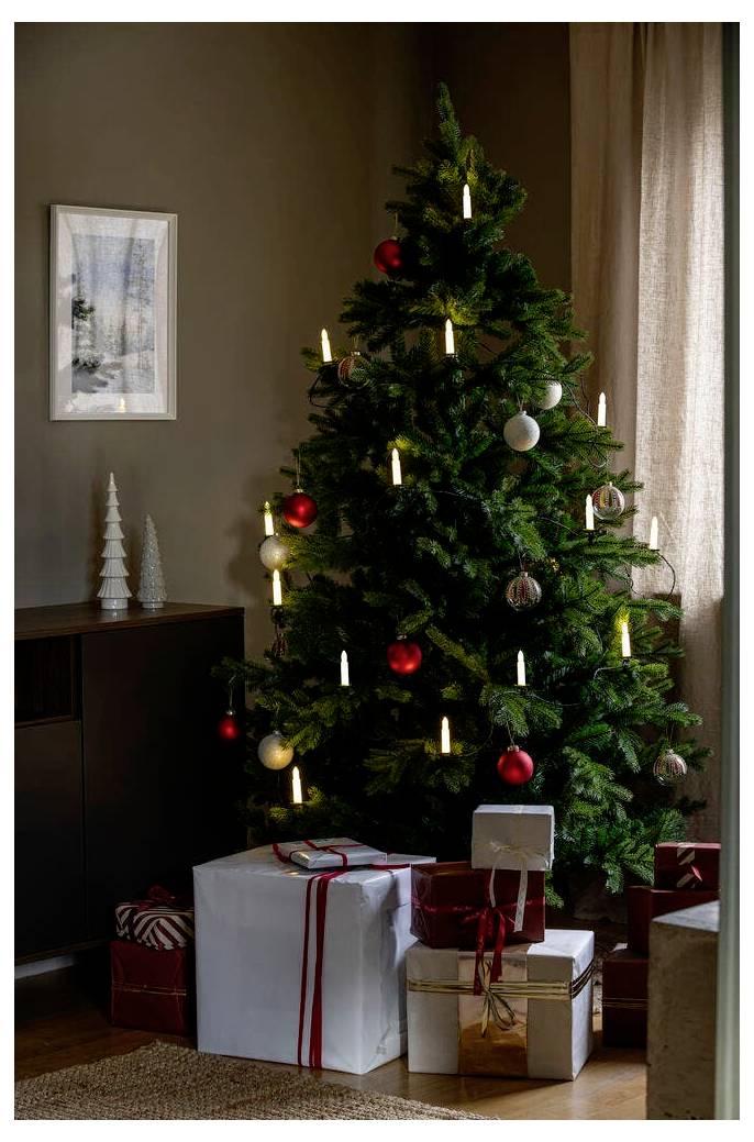 Un sapin de Noël décoré avec des boules rouges et blanches et des lumières en forme de bougies. Des cadeaux emballés dans différents papiers sont disposés en dessous.
