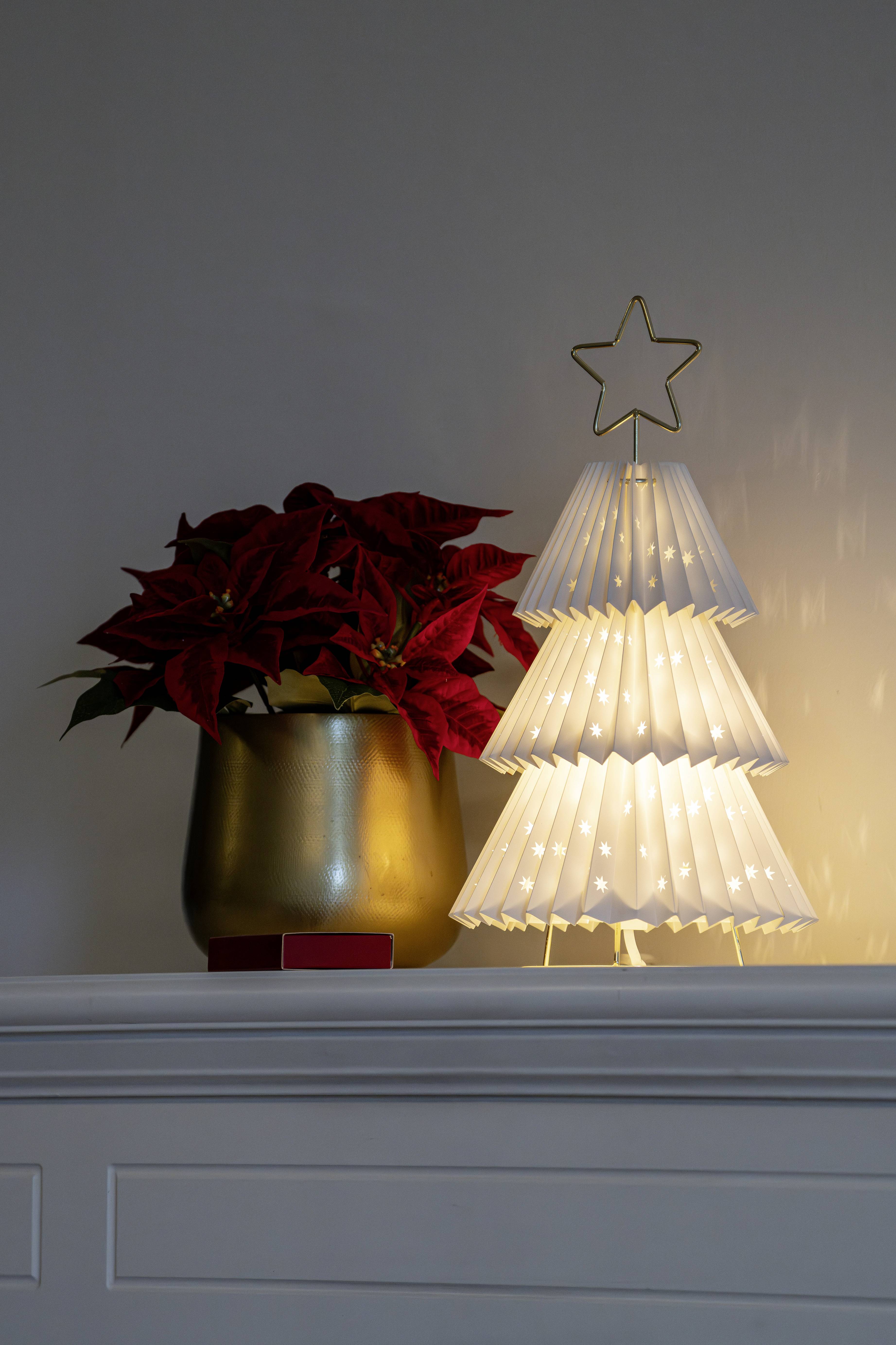 Un petit sapin de Noël en papier lumineux, surmonté d'une étoile, est posé sur une cheminée à côté d'un poinsettia en pot dans un récipient doré.