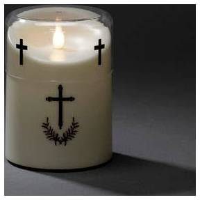 Une bougie blanche allumée avec des décorations de croix noires sur sa surface, projetant une ombre sur la surface grise.