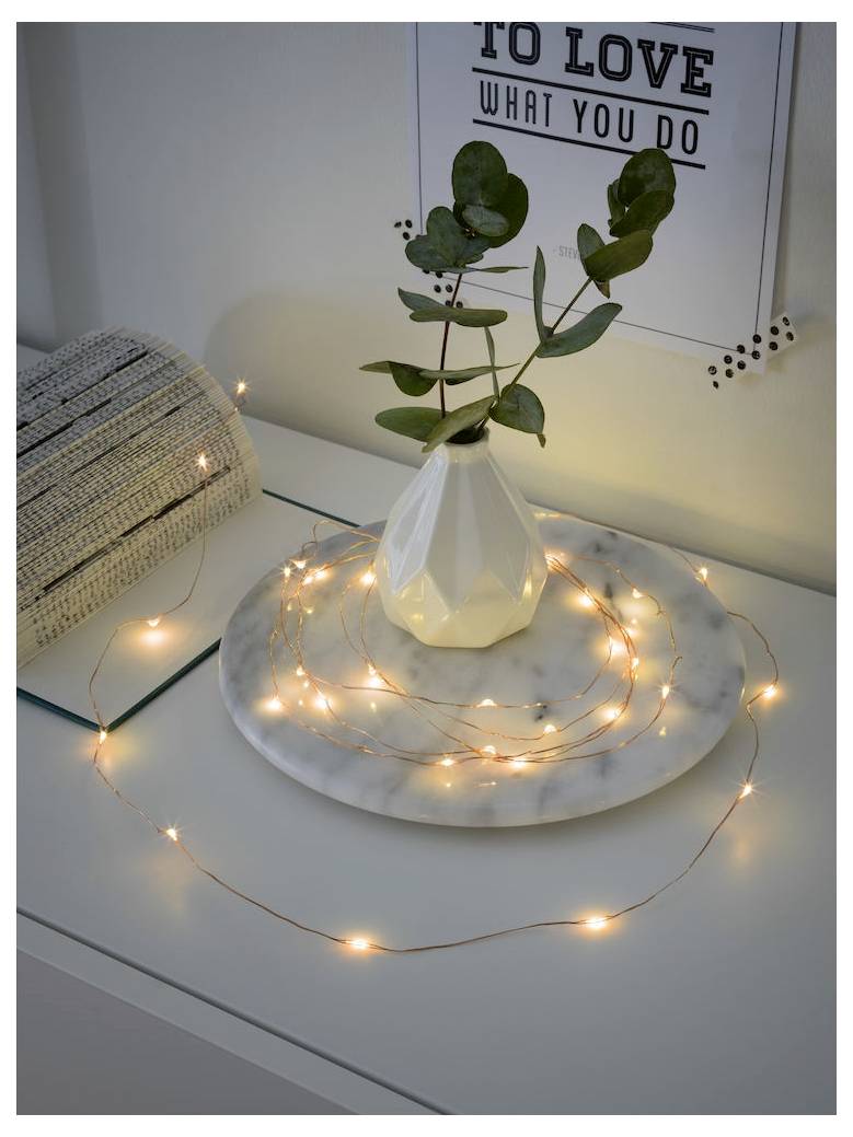 Un vase contenant une branche d'eucalyptus est posé sur une assiette en marbre, entouré de guirlandes lumineuses. Un poster affichant « Aimer ce que l'on fait » est visible.