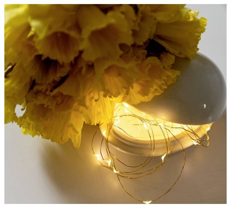 Un bouquet de fleurs jaune vif dans un vase blanc, illuminé par des guirlandes lumineuses chaleureuses, créant une atmosphère chaleureuse et accueillante.