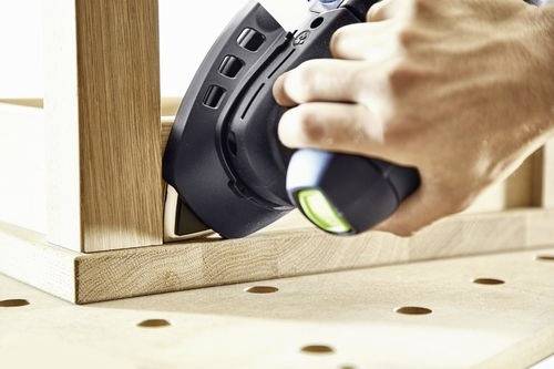 Une personne utilise un outil électrique pour poncer le coin d'un cadre en bois sur un établi, montrant un intérêt pour la menuiserie ou les projets de bricolage.