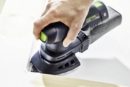 Une personne utilise une ponceuse portative Festool pour lisser une surface en bois. La ponceuse est noire avec des touches vertes.