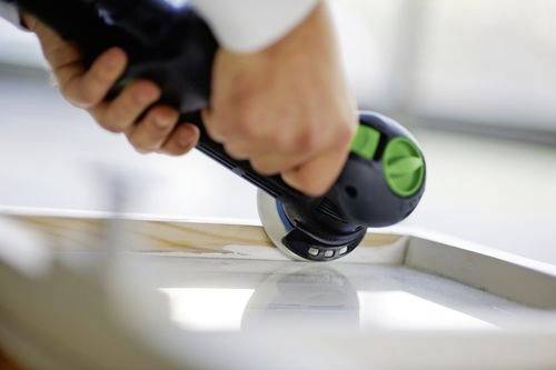 Une personne utilise une ponceuse électrique portative pour lisser la surface d'un cadre en bois, en se concentrant sur la zone d'angle.