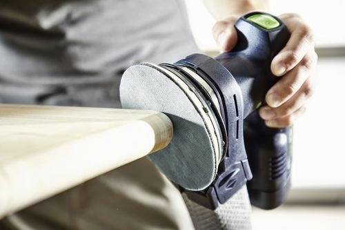 Une personne utilisant une ponceuse électrique pour lisser le bord d'une surface en bois, en se concentrant sur l'artisanat et la précision.