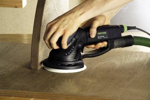 Une personne ponce une surface en bois avec une ponceuse électrique Festool. La ponceuse est en contact avec le bois, en lissant le grain.