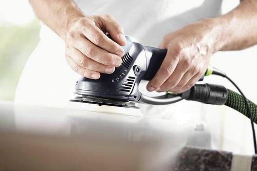 Des mains manient une ponceuse électrique sur une surface lisse, mettant en valeur un travail de menuiserie précis ou de finition de surface.