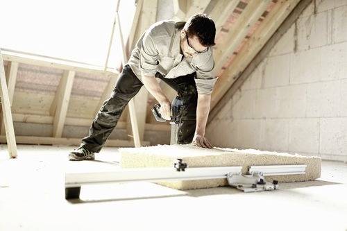 Un homme utilise un outil électrique pour couper un morceau de bois dans un grenier en cours de rénovation, mettant en évidence une tâche d'amélioration de l'habitat.