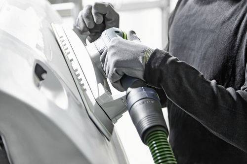 Personne utilisant une ponceuse sur une portière de voiture, portant des gants de protection. L'accent est mis sur le processus de ponçage, mettant en valeur le travail de réparation automobile.