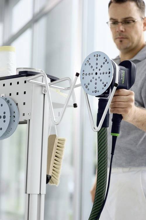 Un homme utilisant un grand outil électrique à tête ronde, fixé à un chariot contenant divers produits de nettoyage, dans un espace lumineux et moderne.
