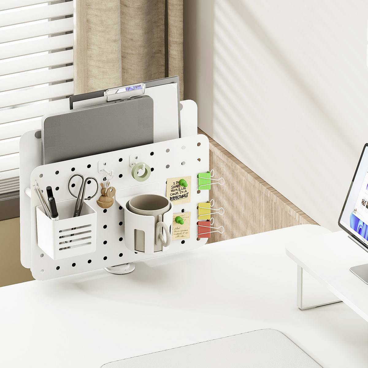 'Un organisateur de bureau blanc fixé à une cloison contient des fournitures de bureau, un bloc-notes et des plantes, à côté d'un ordinateur portable sur un bureau blanc.'
