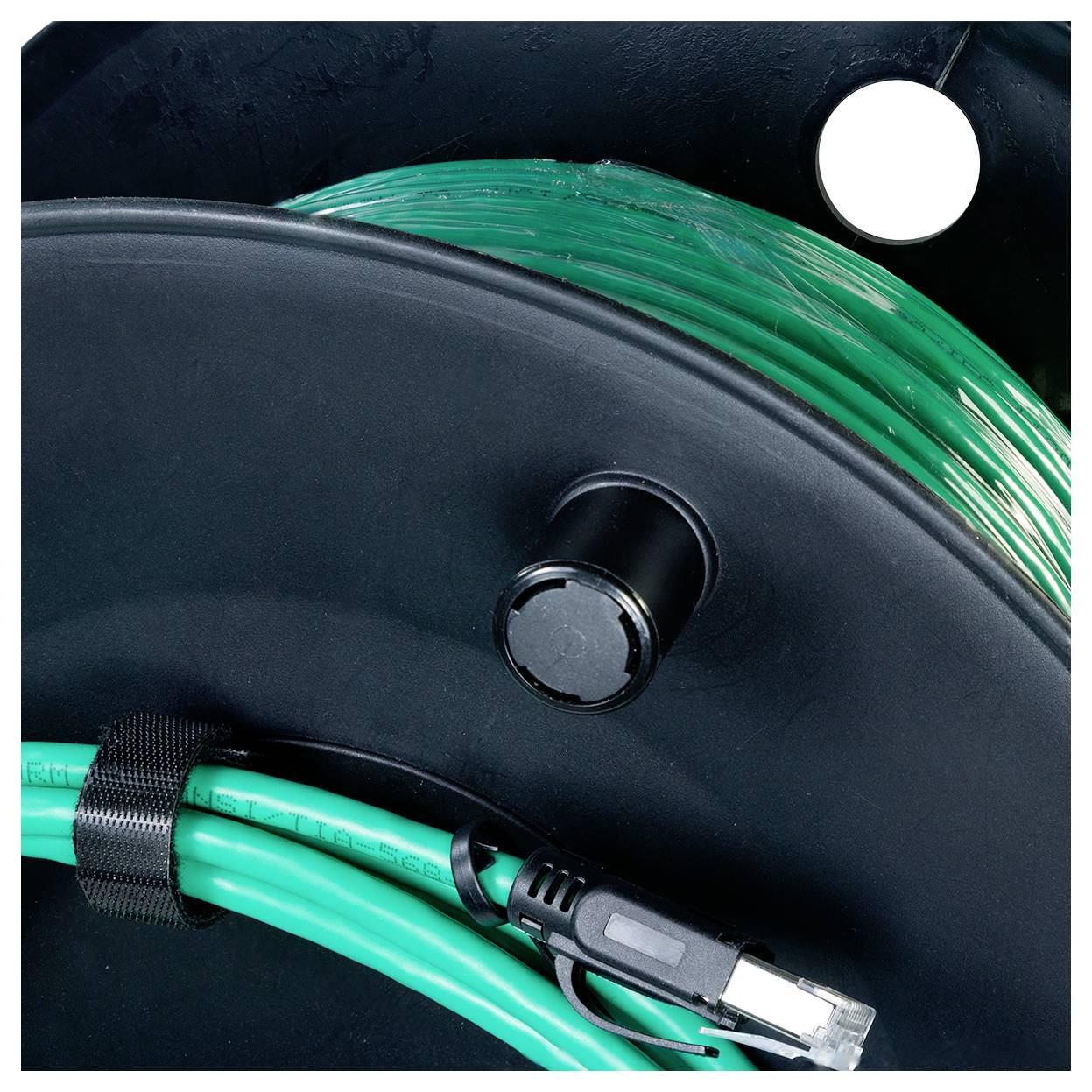 Un câble vert enroulé avec un connecteur est enroulé autour d'une bobine noire, avec une portion supplémentaire visible sous une sangle fixée.