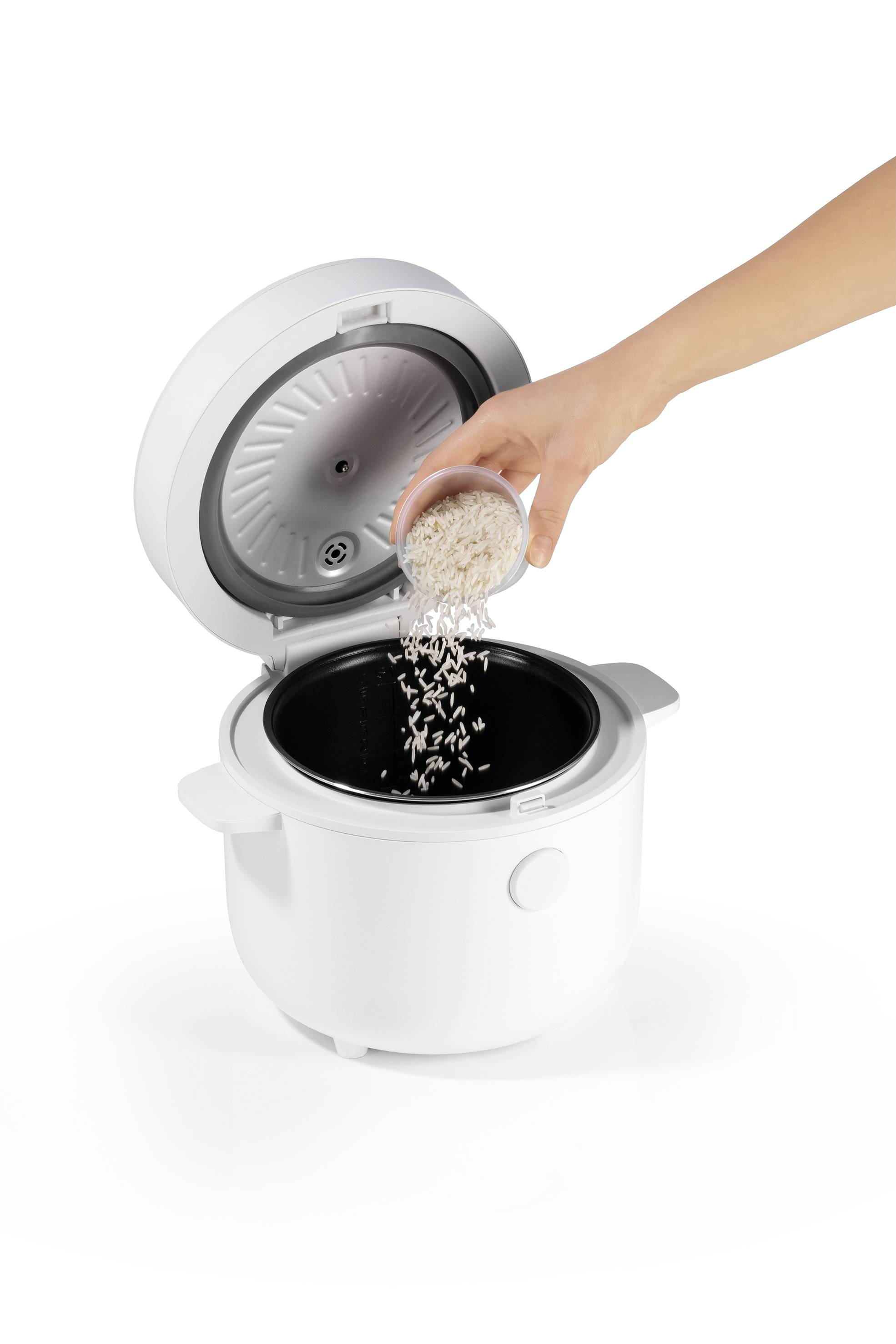 Une personne verse du riz dans une cooker à riz blanche ouverte, mettant en évidence le processus de préparation.