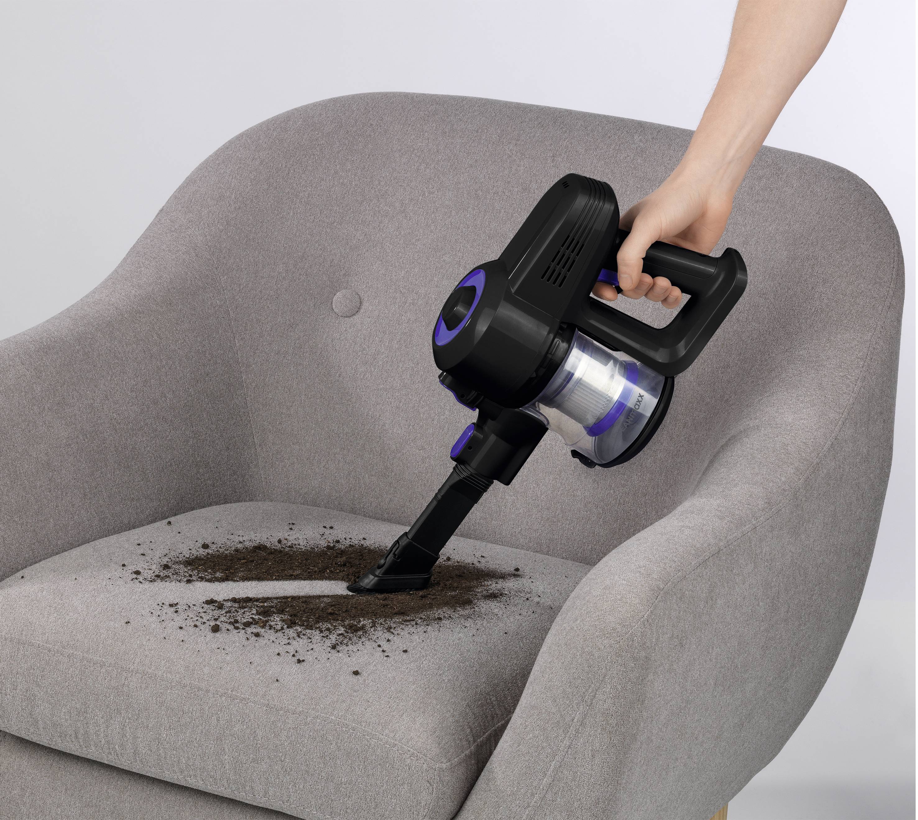 Une personne utilise un aspirateur à main pour éliminer la saleté d'une chaise rembourrée grise, illustrant un nettoyage efficace.