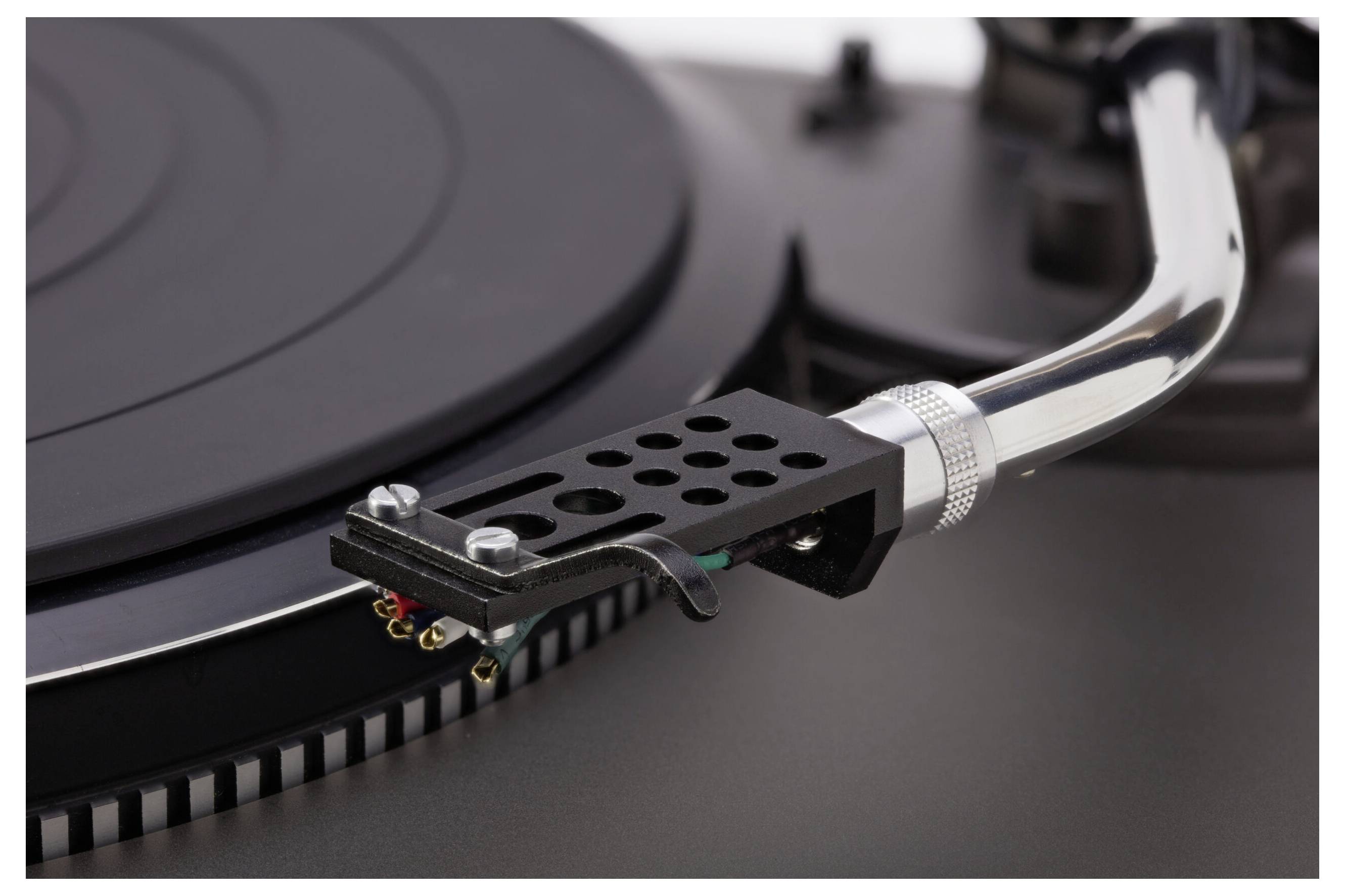 Un gros plan sur le bras de lecture et la cellule d'un tourne-disque positionnés au-dessus du disque vinyle, révélant les détails intricats de la conception et des composants.