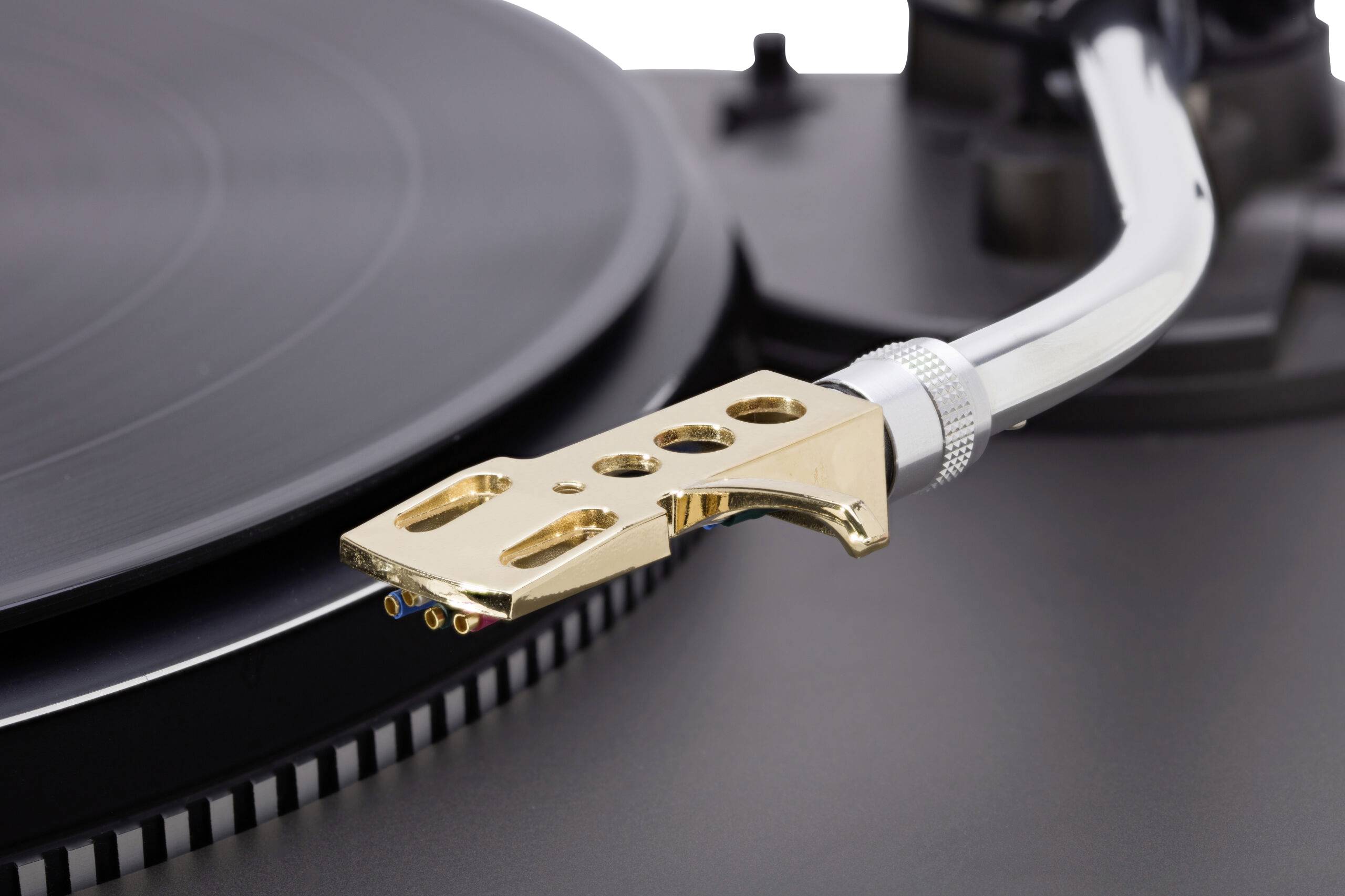 Gros plan sur l'aiguille et le bras de lecture d'une platine vinyle sur un disque noir, mettant en valeur le capot de lecture doré sur un arrière-plan flou.