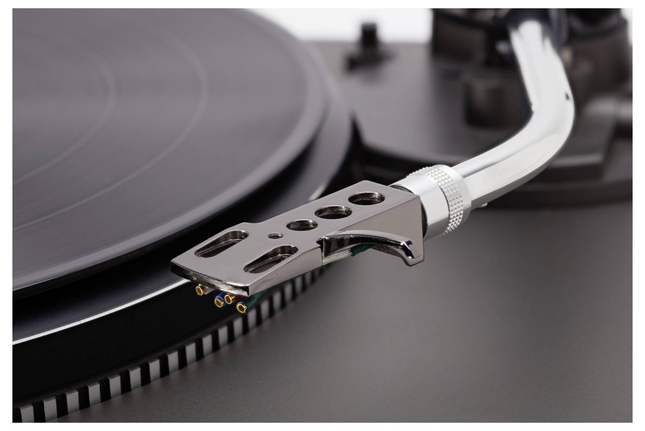 Un gros plan sur un tourne-disque vinyle, avec mise au point sur le bras de lecture et l'aiguille suspendus au-dessus d'un disque noir en rotation.