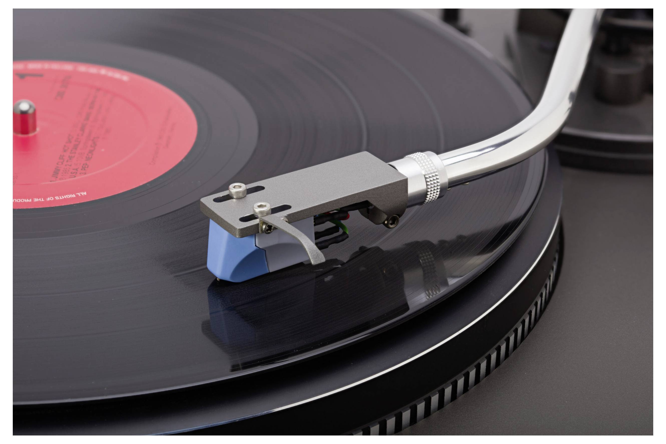 Un gros plan d'une platine tourne-disque jouant un disque vinyle avec une étiquette rouge. La pointe de lecture est posée sur le disque, capturant précisément les sillons pour la lecture.