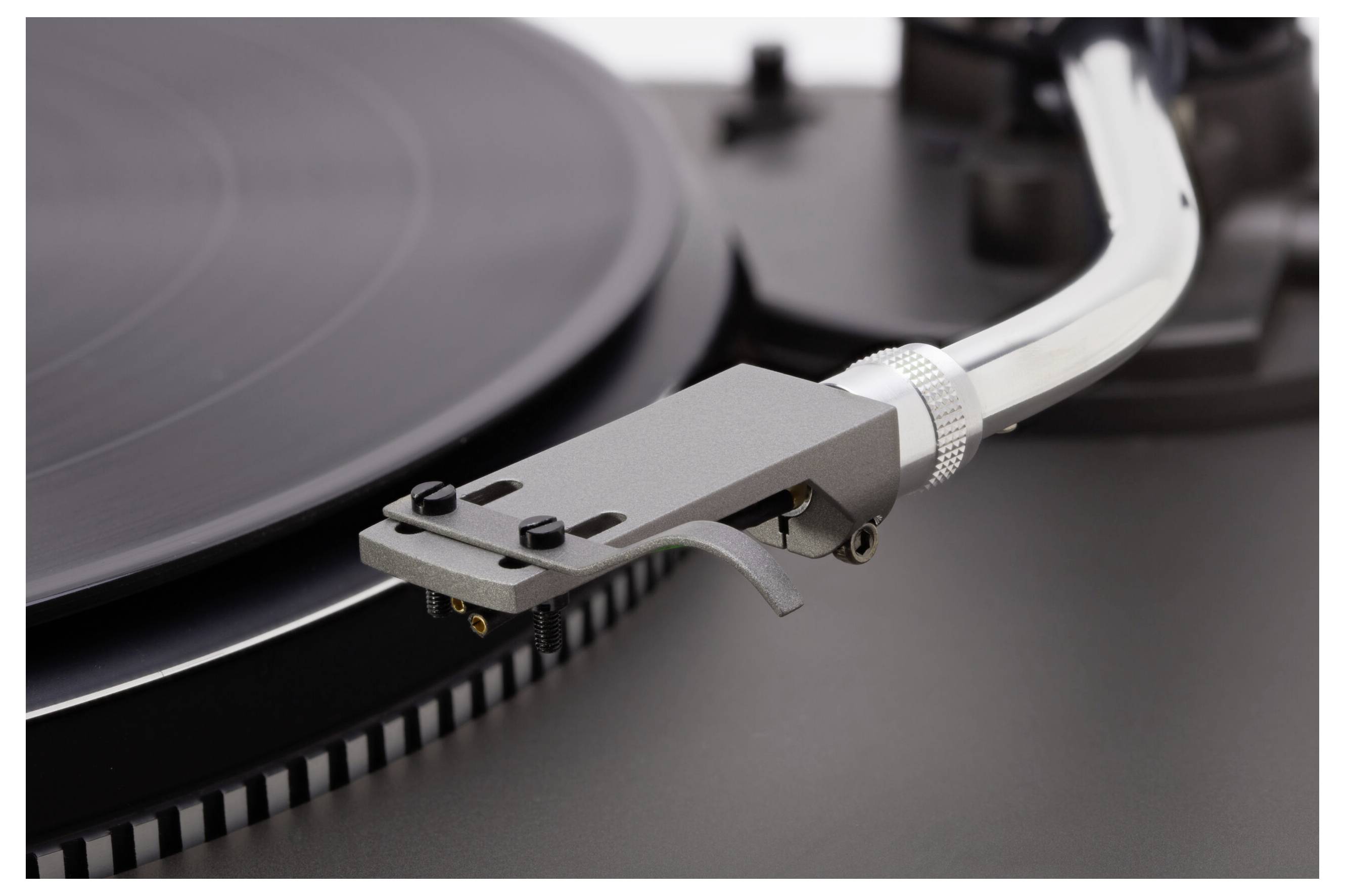 Un gros plan du bras de lecture et du stylet d'un tourne-disque vinyle, positionnés près du bord d'un disque vinyle noir, prêts à faire jouer de la musique.