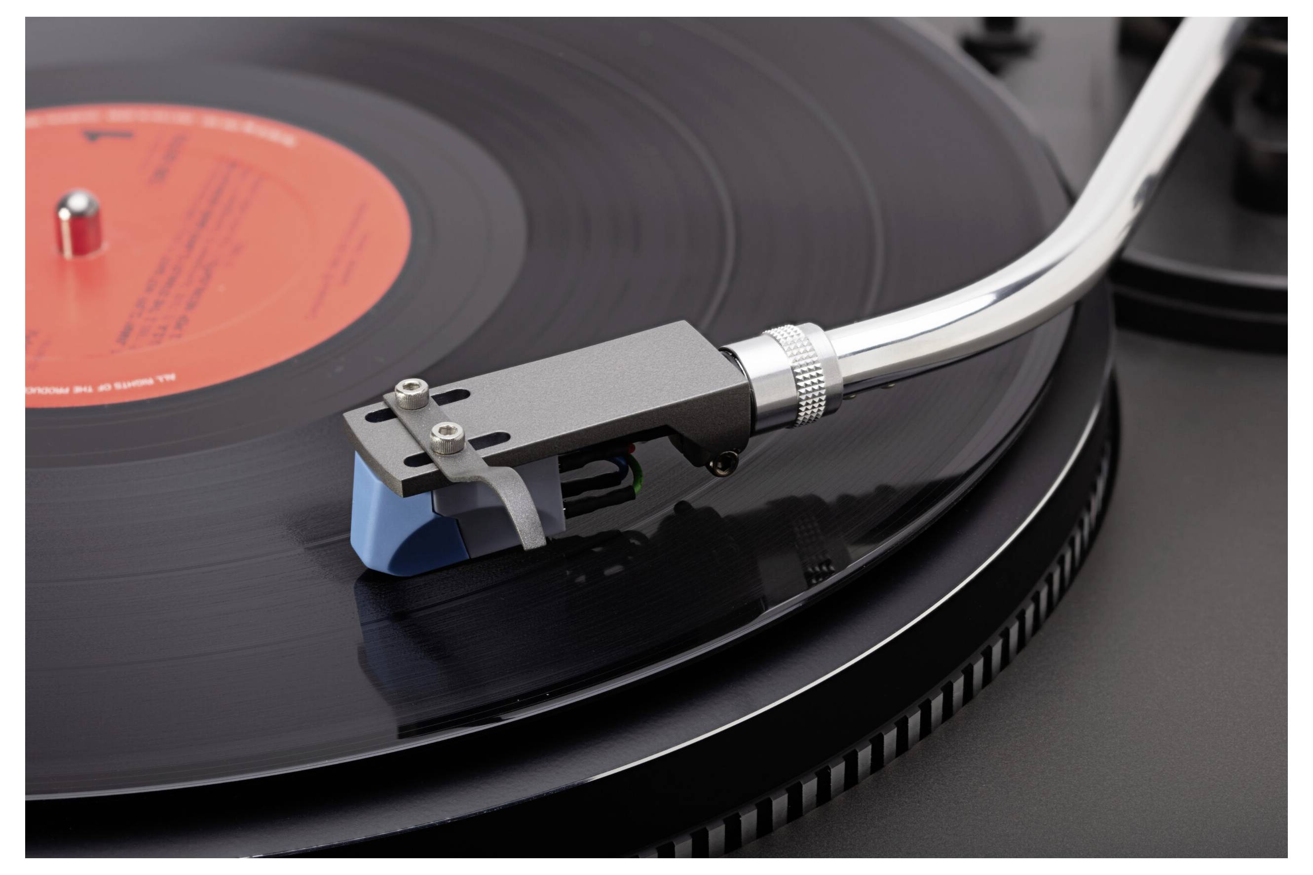 Un disque vinyle tournant sur une platine tourne-disque, le bras de lecture et la pointe en contact avec le disque en rotation.