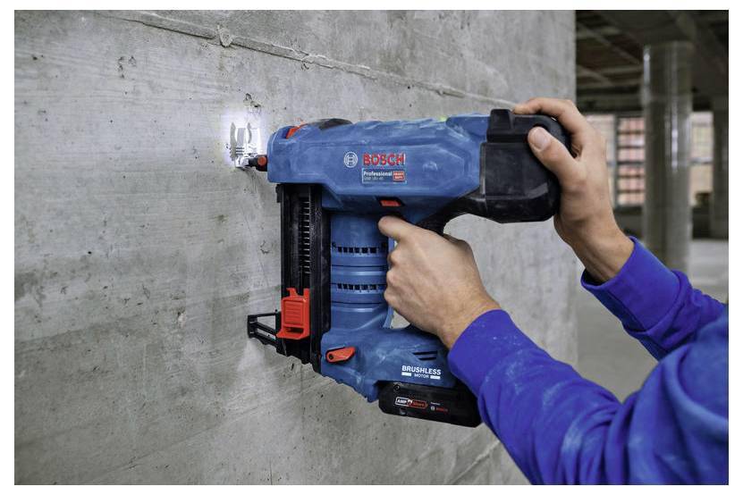 Personne utilisant un cloueur pneumatique bleu et noir pour fixer du matériau sur un mur en béton dans un environnement industriel.