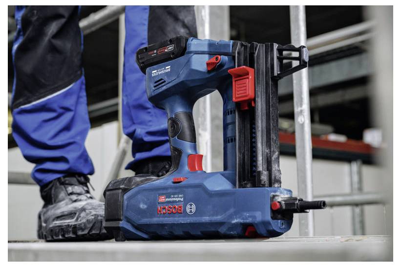 Une personne portant des bottes de travail et un pantalon bleu se tient près d'un cloueur sans fil Bosch sur un chantier de construction, soulignant l'utilisation d'outils dans le bâtiment.