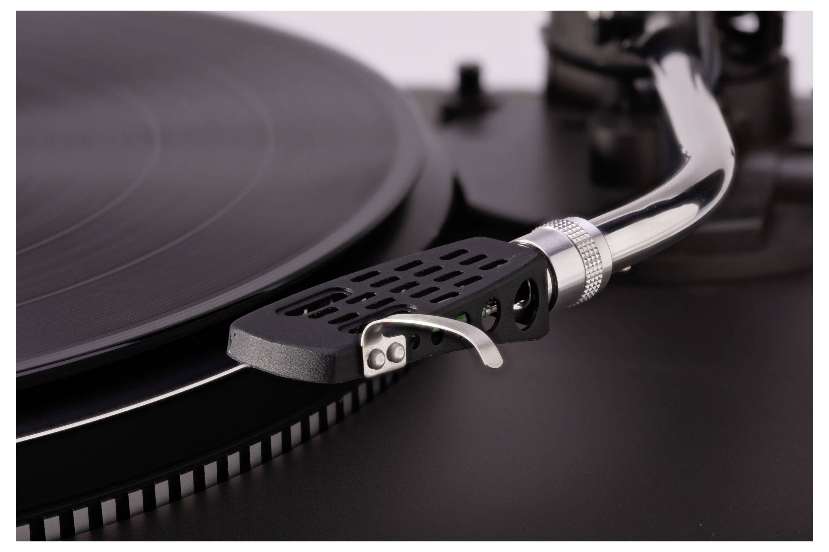 Un gros plan de l'aiguille et du bras de lecture d'une platine vinyle reposant sur un disque vinyle, mettant en valeur les sillons et les détails du tourne-disque.