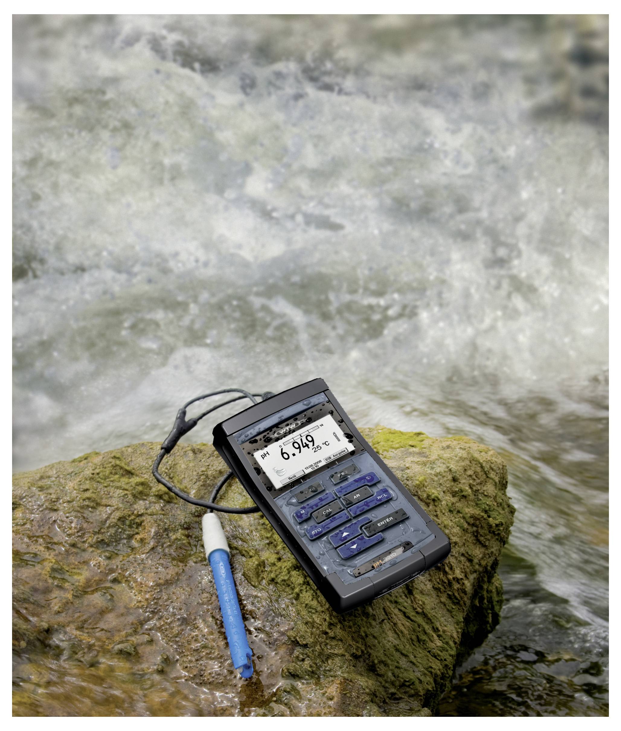 Un mètre de qualité de l'eau et un stylo-sonde bleu reposent sur un rocher à côté d'un ruisseau coulant, affichant une lecture de pH de 6,946.