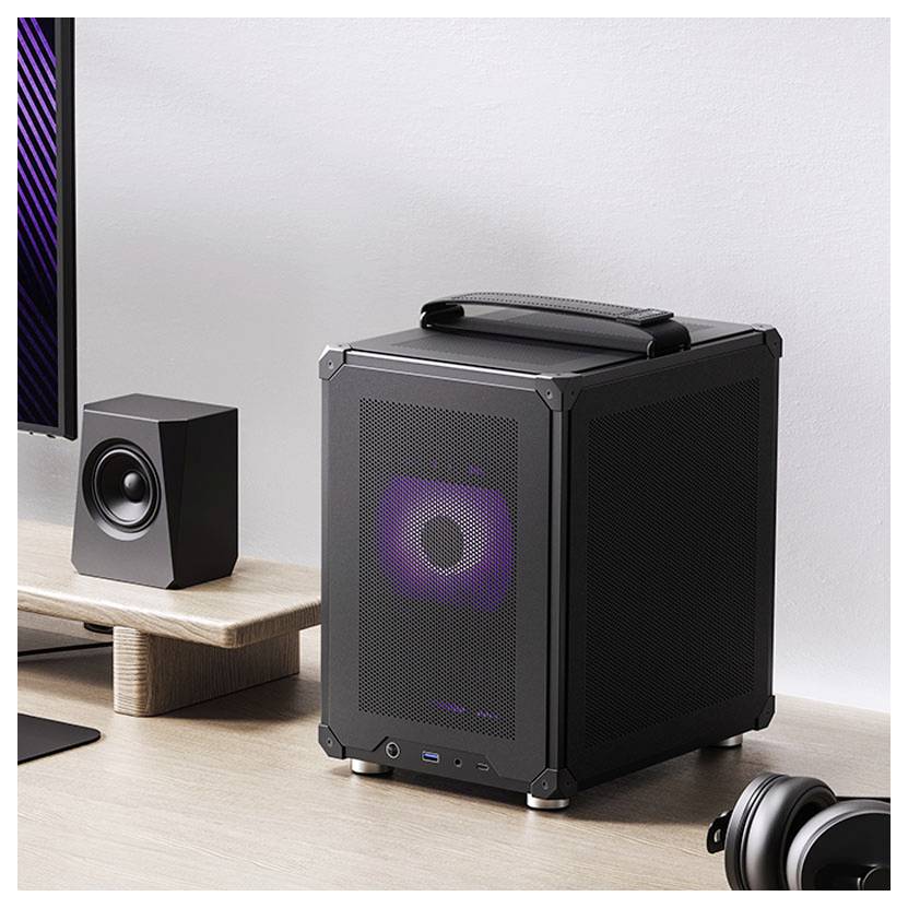 Un petit ordinateur de bureau cubique doté d'un panneau avant en maille avec un éclairage RVB est posé sur un bureau en bois à côté d'un haut-parleur.