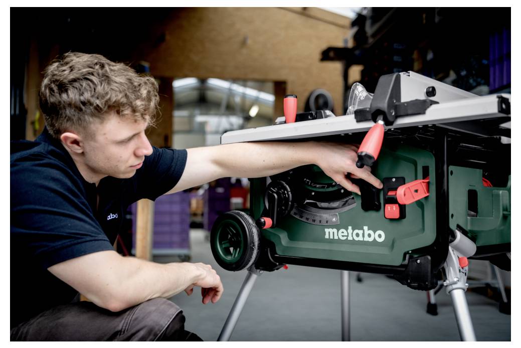 Personne ajustant une scie sur table Metabo à l'intérieur d'un atelier, concentrée sur les commandes de la machine avec une expression attentive.