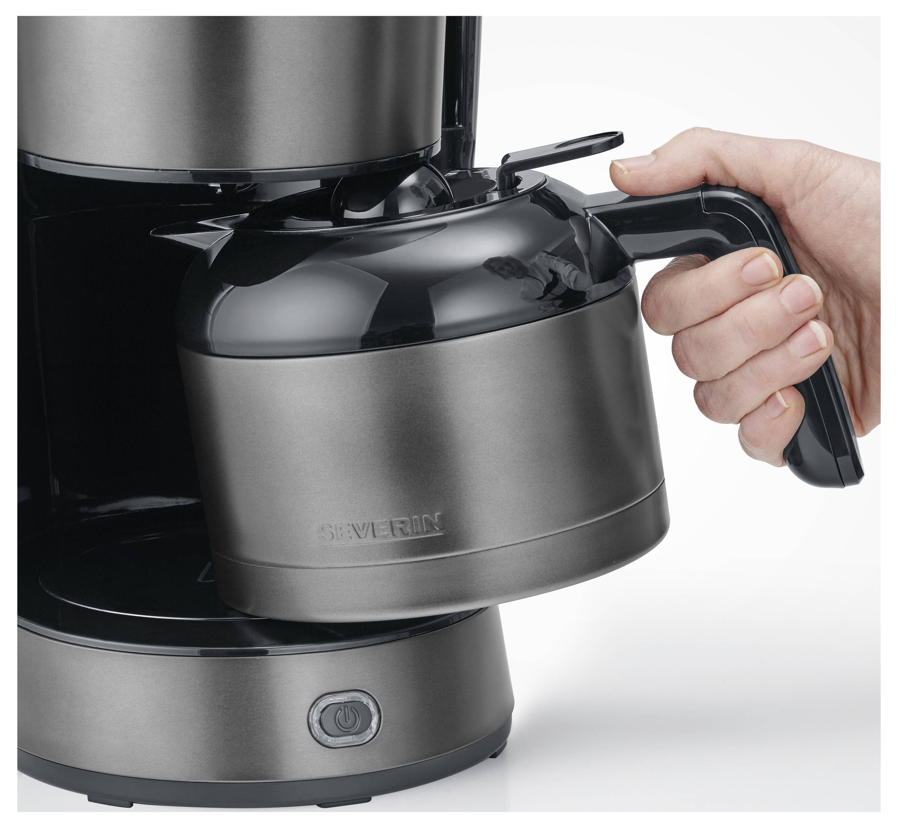 Une main tient la poignée d'une carafe à café métallique, la plaçant dans une machine à café sur un comptoir de cuisine.