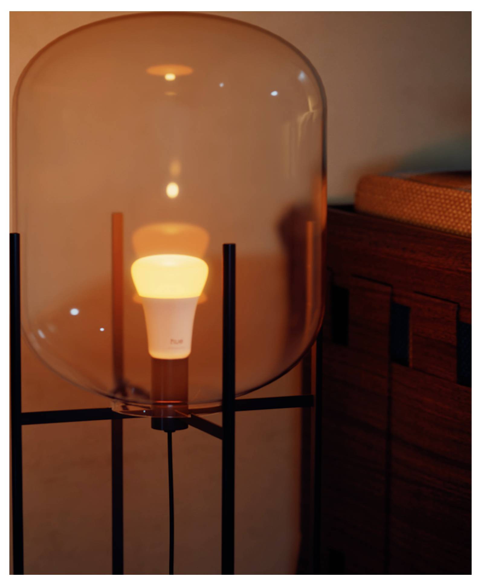 Une ampoule lumineuse à l'intérieur d'une lampe moderne en verre transparent, placée à côté d'un meuble en bois dans une pièce doucement éclairée.