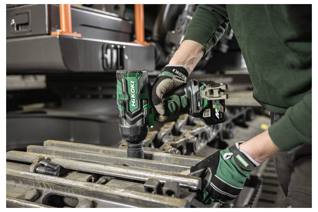 Une personne portant des gants utilise une clé à chocs sans fil Hikoki sur des pièces de machinerie métalliques, indiquant un environnement de réparation ou de maintenance industrielle.