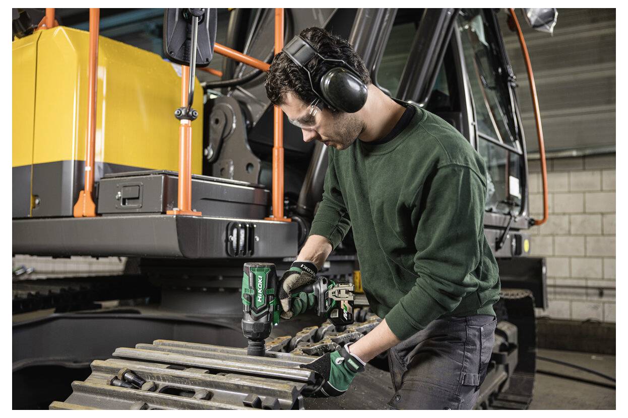 Une personne portant une protection auditive utilise un outil électrique sur des machines lourdes, en se concentrant sur la maintenance dans un environnement industriel.