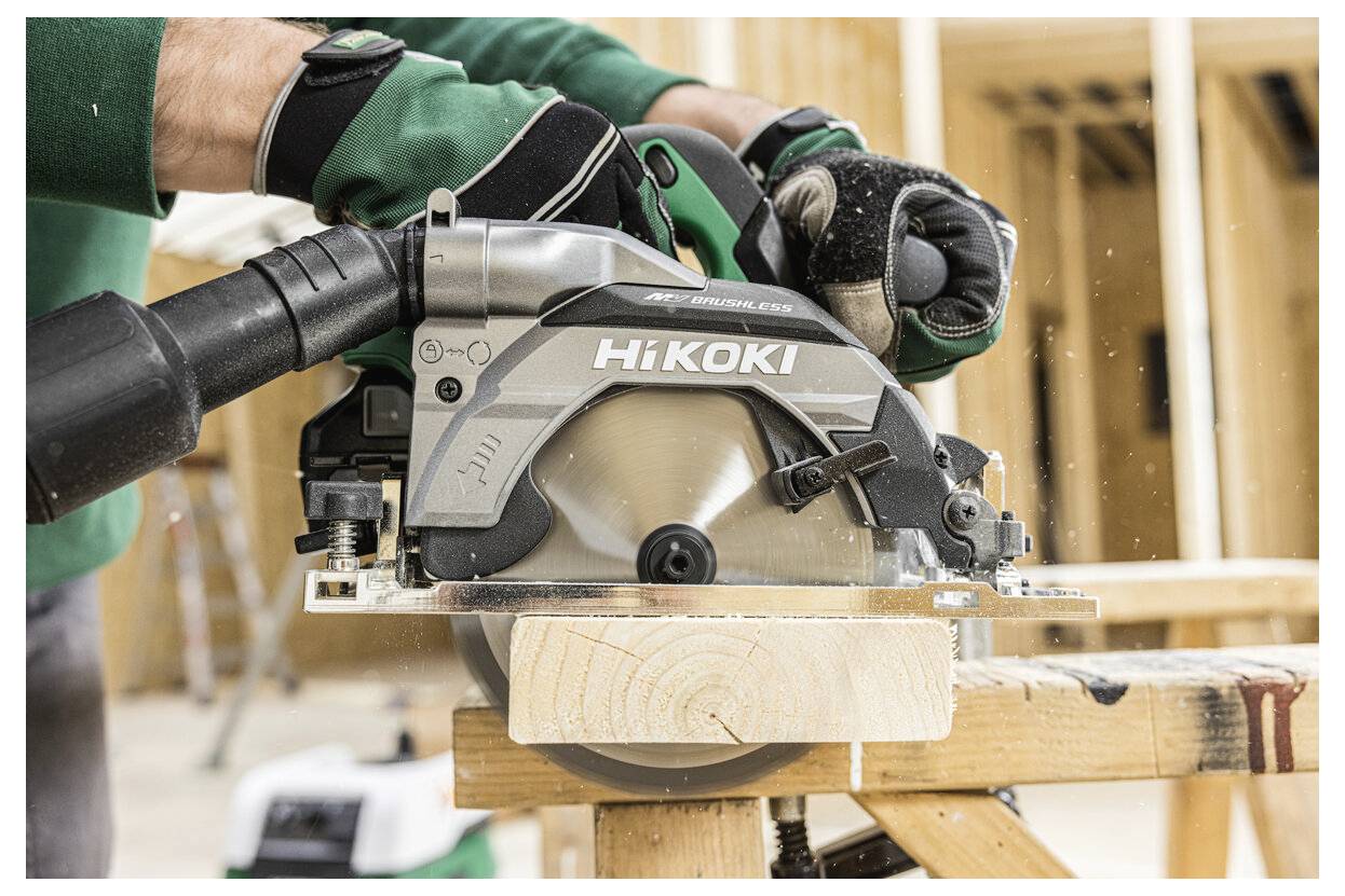 Une personne équipée d'un équipement de protection utilise une scie circulaire Hikoki pour couper une planche en bois sur un tréteau dans un environnement de construction.