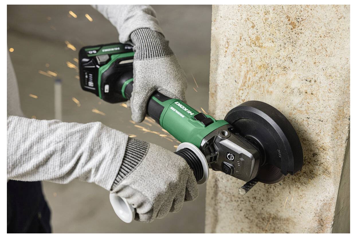 Une personne portant des gants utilise une meuleuse d'angle sans fil pour lisser le bord d'une surface en béton, avec des étincelles visibles autour de la meuleuse.