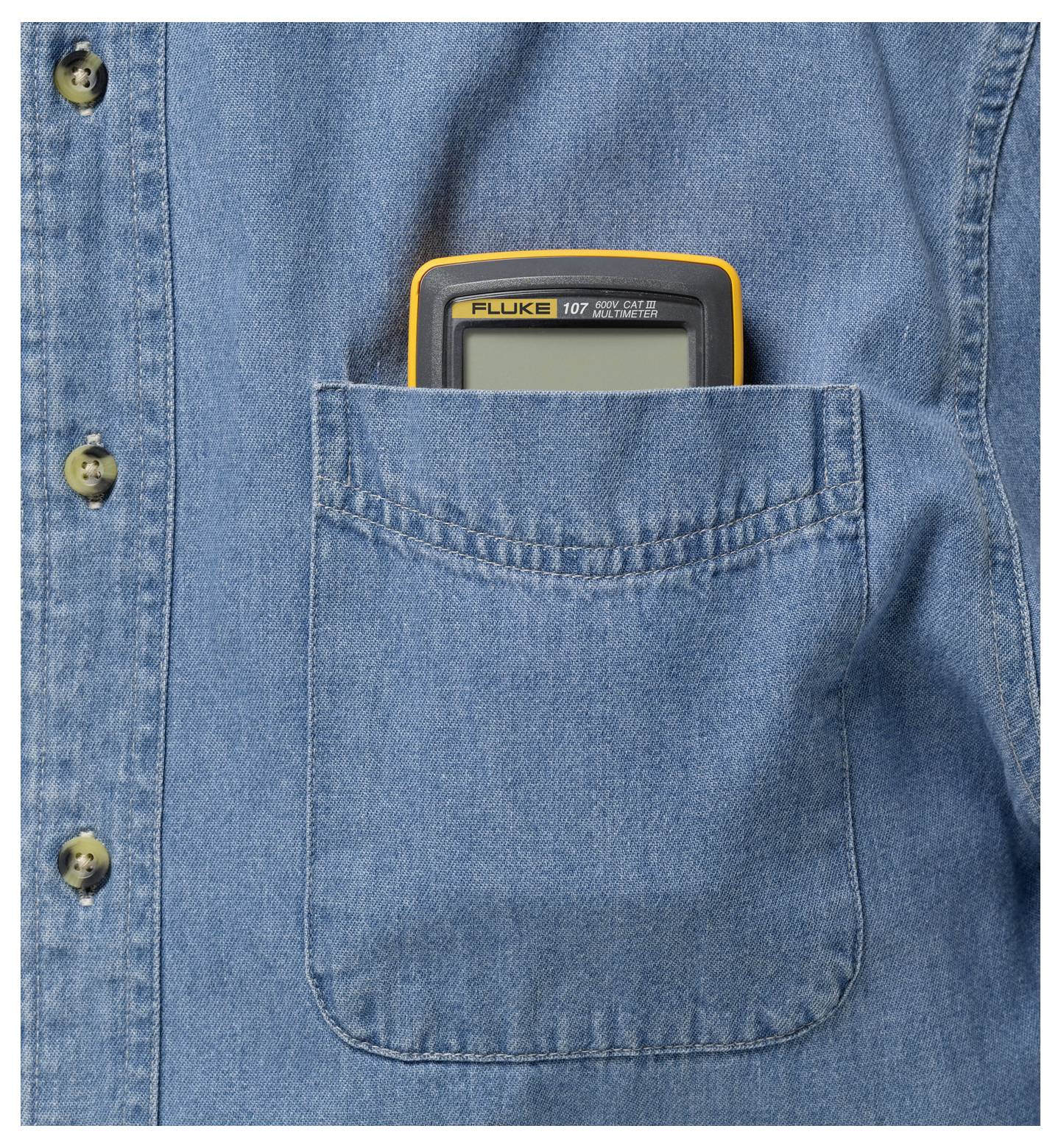 Un multimètre au bord jaune est rangé dans la poche de poitrine d'une chemise en jean bleu.