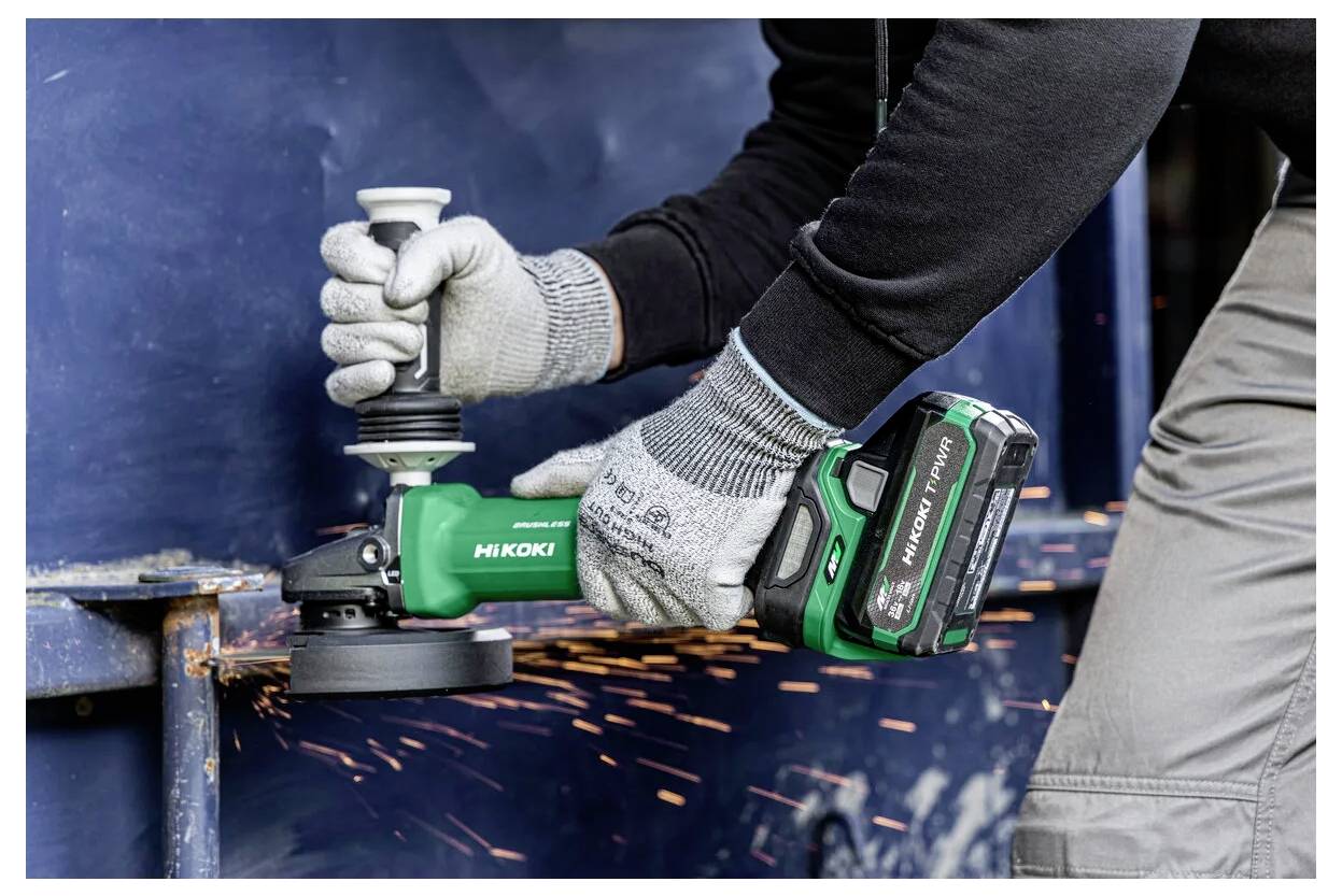 Personne utilisant un outil électrique Hitachi pour meuler du métal, portant des gants et provoquant des projections d'étincelles.