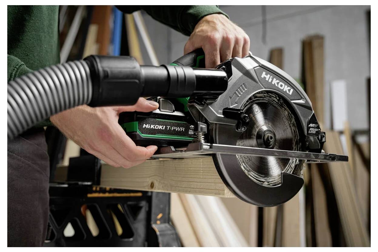 Une personne utilisant une scie circulaire HiKOKI pour couper une planche en bois dans un atelier, avec divers morceaux de bois en arrière-plan.