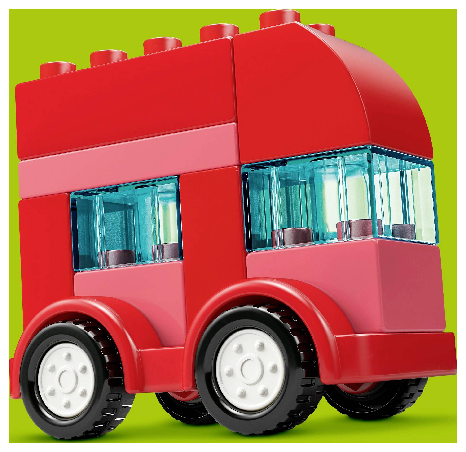 Un bus jouet rouge fabriqué en briques de plastique emboîtables, posé sur un fond vert, doté de grandes fenêtres et de roues noires.