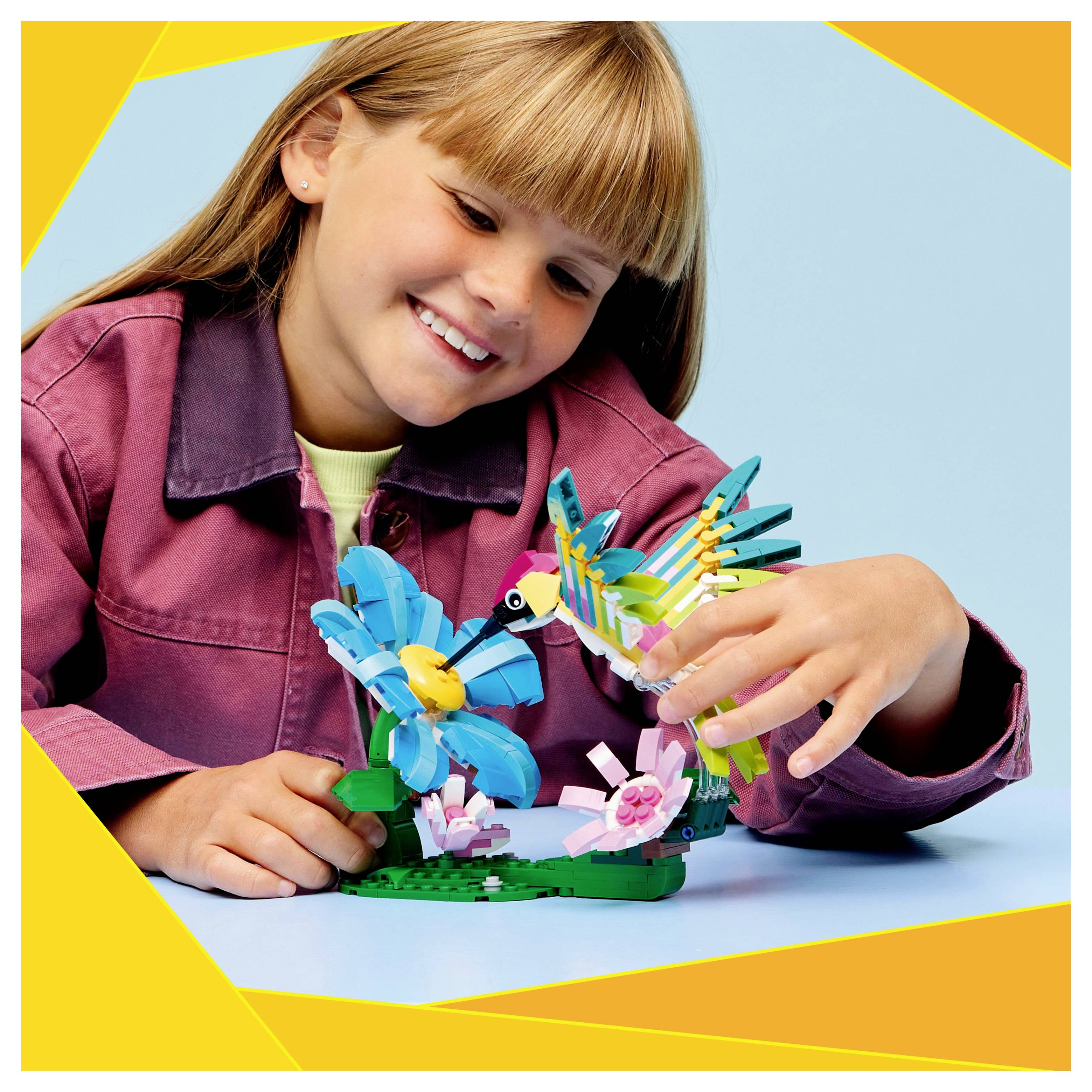 Un enfant sourit en assemblant un ensemble LEGO coloré de fleurs et d'oiseaux, mettant en valeur la créativité et le jeu.
