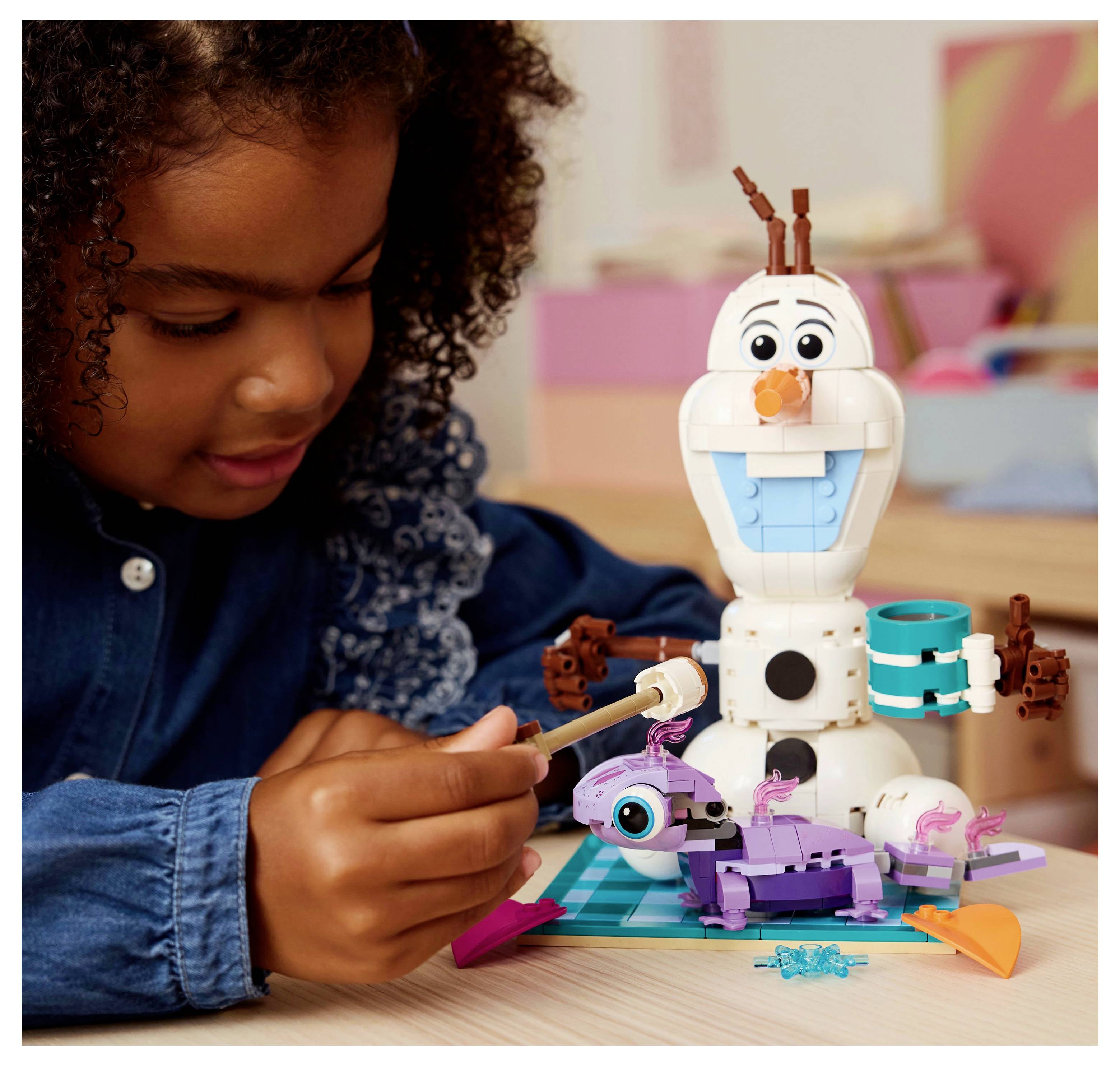 Un enfant assemble un robot jouet coloré comprenant un bonhomme de neige et une petite créature violette, démontrant sa créativité et son esprit de jeu dans une pièce chaleureuse.