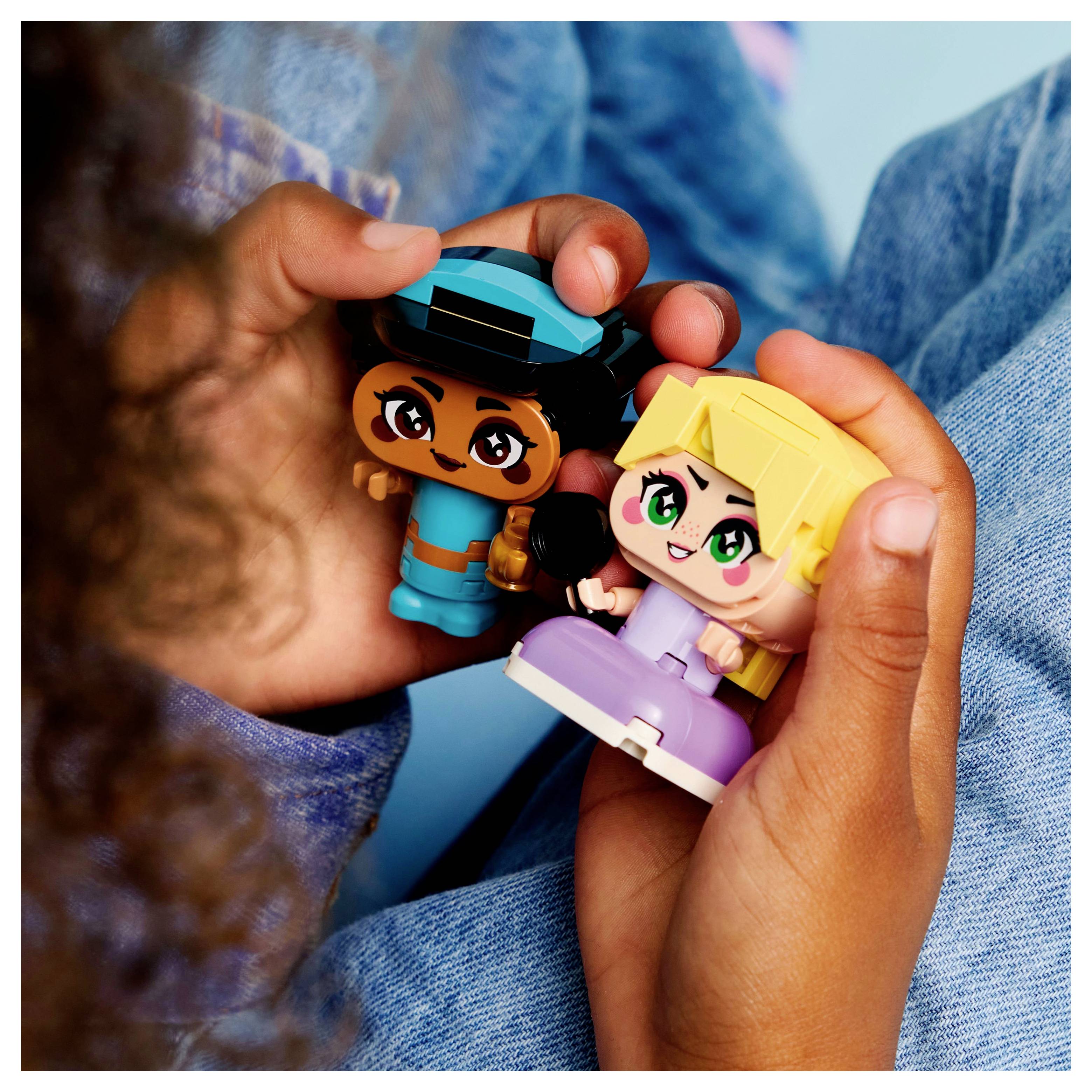 Deux enfants tenant des figurines de jouets colorées, l'un portant une tenue bleue avec un chapeau et l'autre vêtu d'un ensemble violet clair, assis sur une surface bleue.