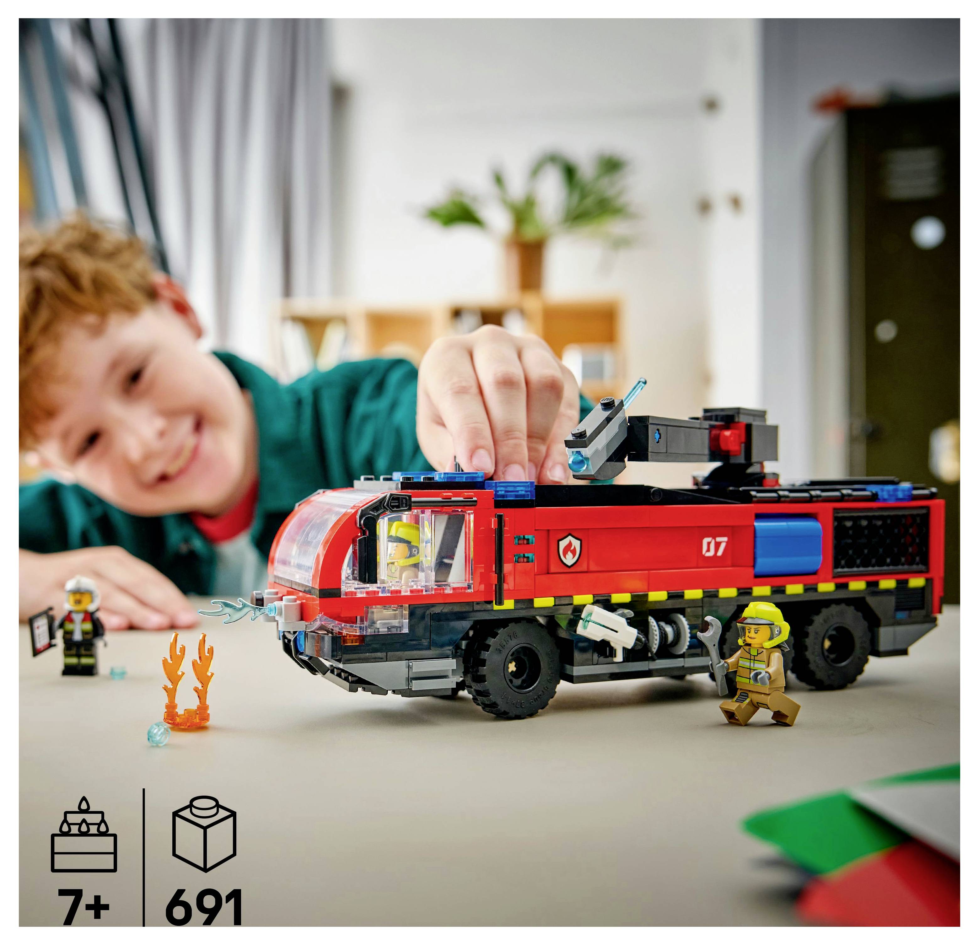 Un enfant jouant avec un ensemble LEGO de camion de pompiers, comprenant des pompiers et des flammes. L'image indique une recommandation d'âge « 7+ » et un nombre de pièces de « 691 ».