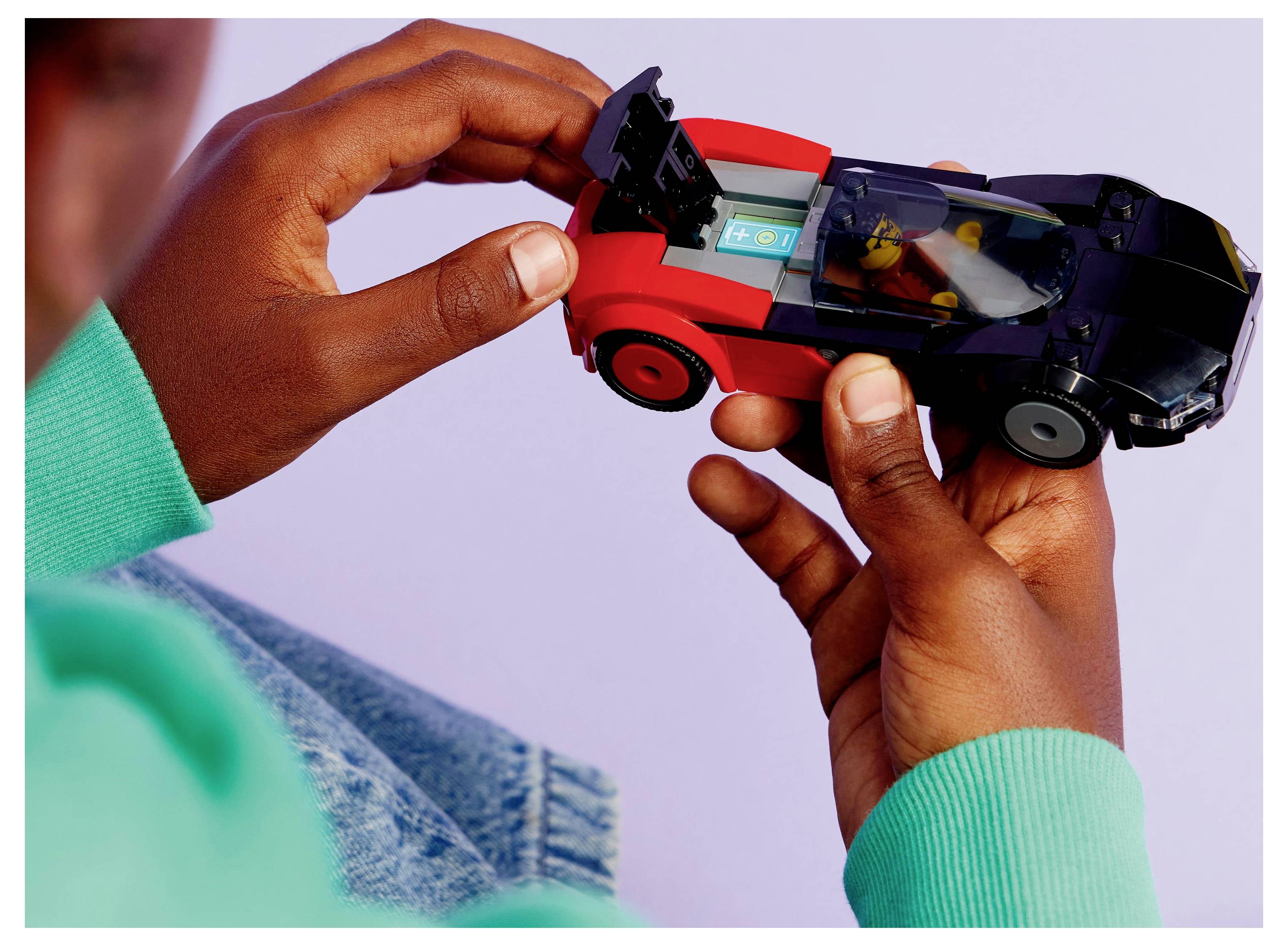 Un enfant jouant avec une petite voiture de jouet rouge et noire, en se concentrant sur les détails avec une figurine miniature assise à l'intérieur, sur un fond doux.
