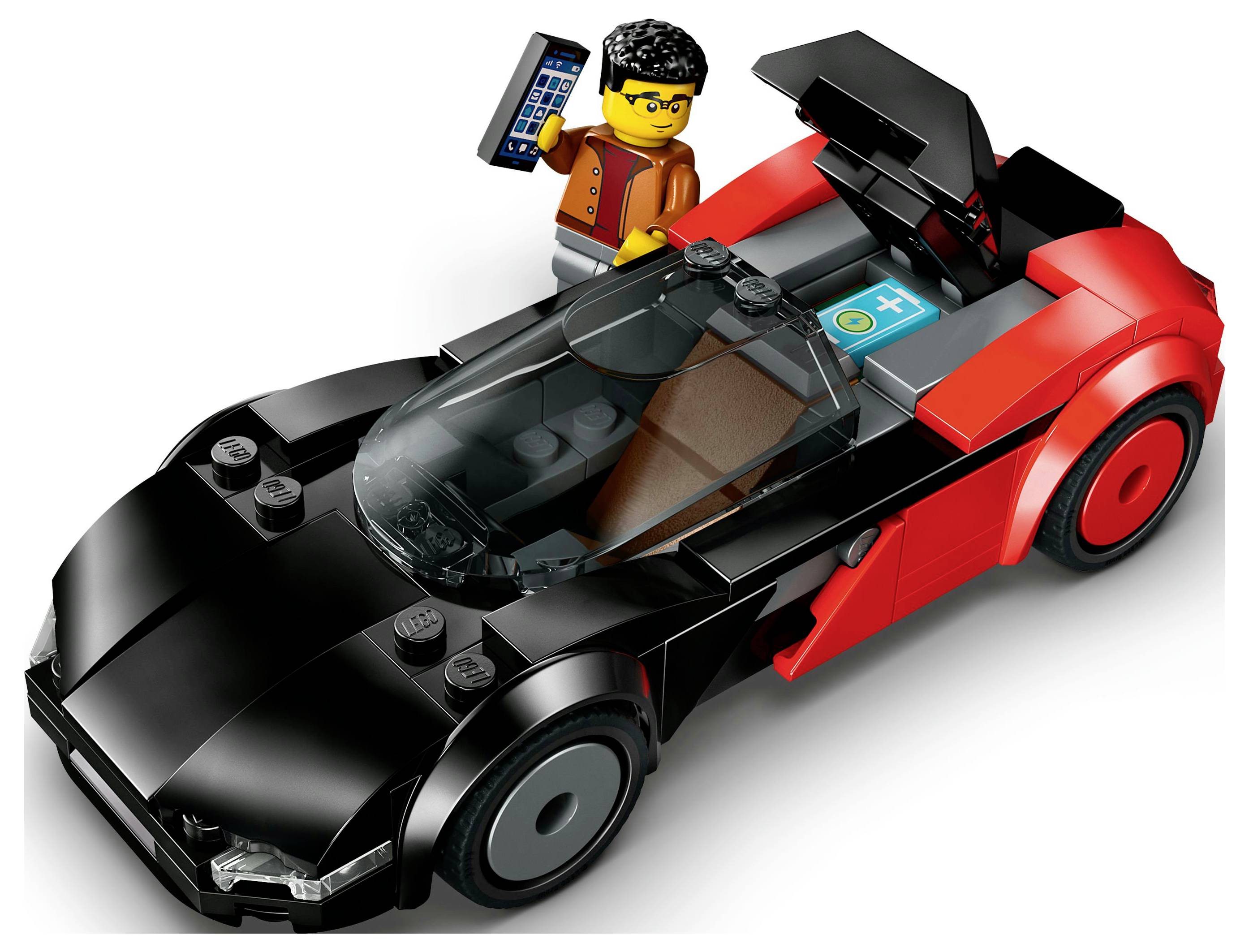 Une figurine LEGO portant des lunettes se tient à côté d'un modèle de voiture de sport noir et rouge, tenant un petit appareil. La voiture présente un design élégant.
