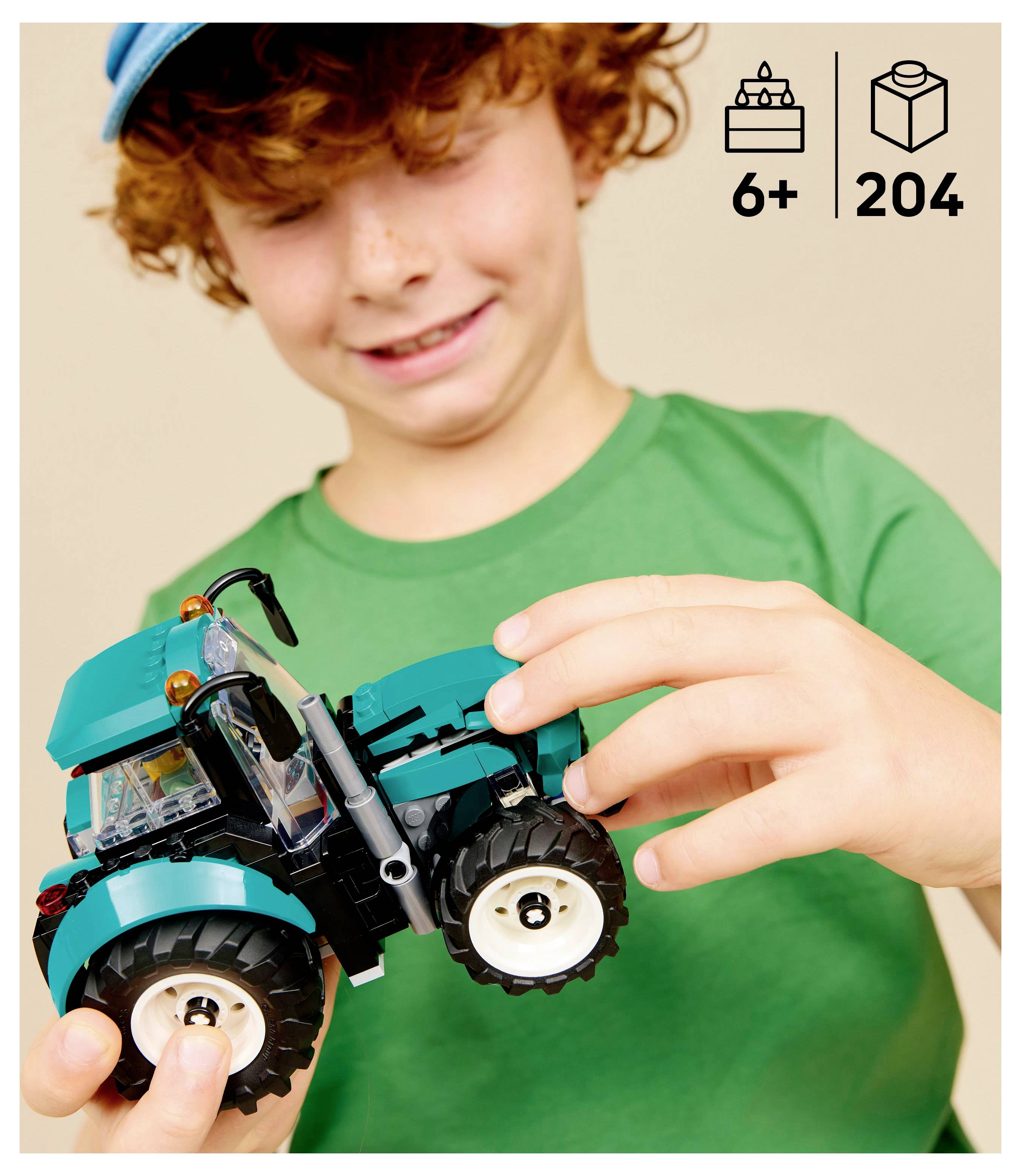 Un enfant portant un t-shirt vert tient un jouet de tracteur bleu avec de grandes roues. L'image met en évidence l'âge '6+' et le nombre de pièces '204' dans le coin.