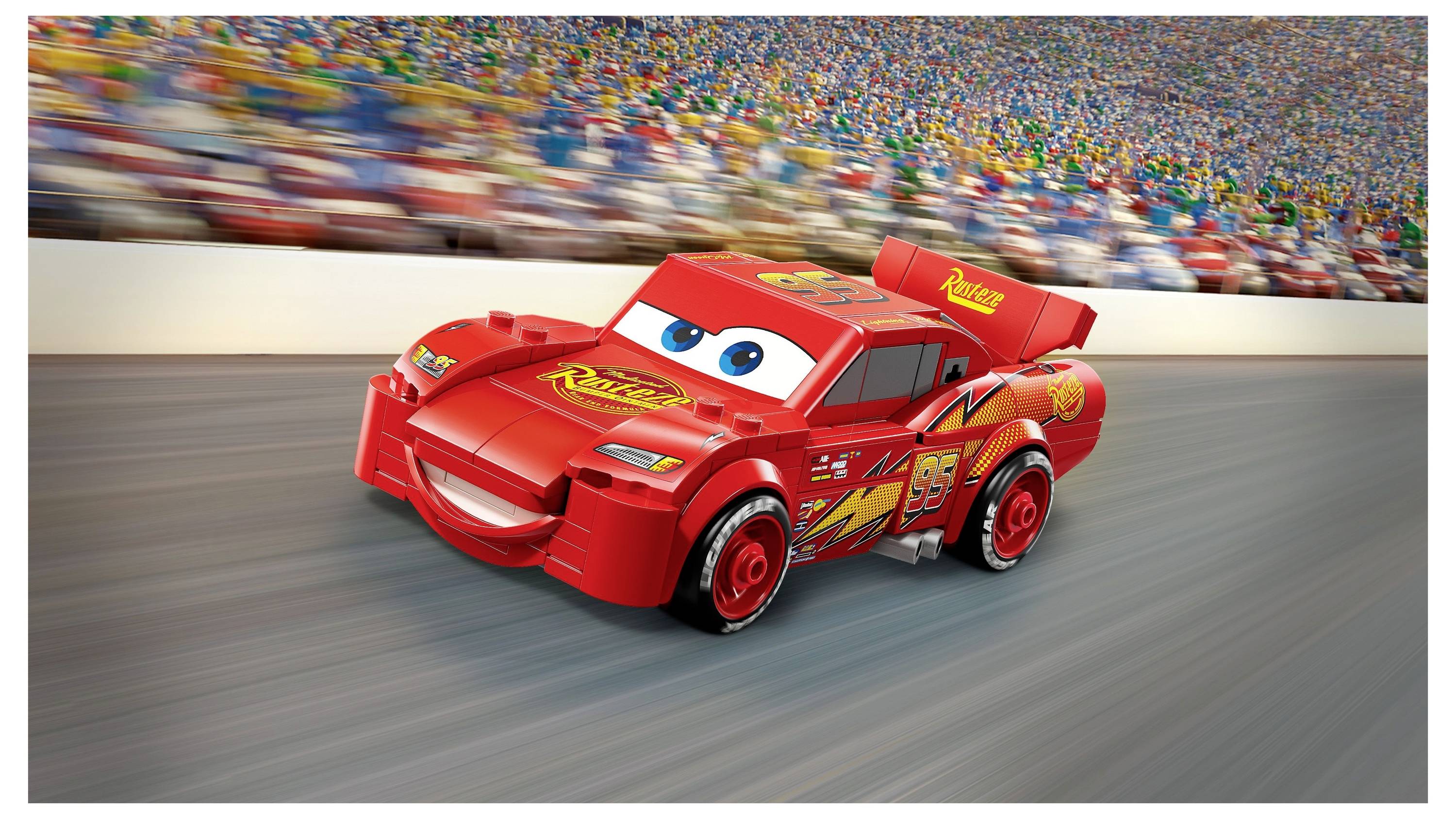 Une voiture de course miniature avec des yeux et une bouche, ressemblant à un personnage de film, file sur un circuit de course avec une foule floue en arrière-plan.