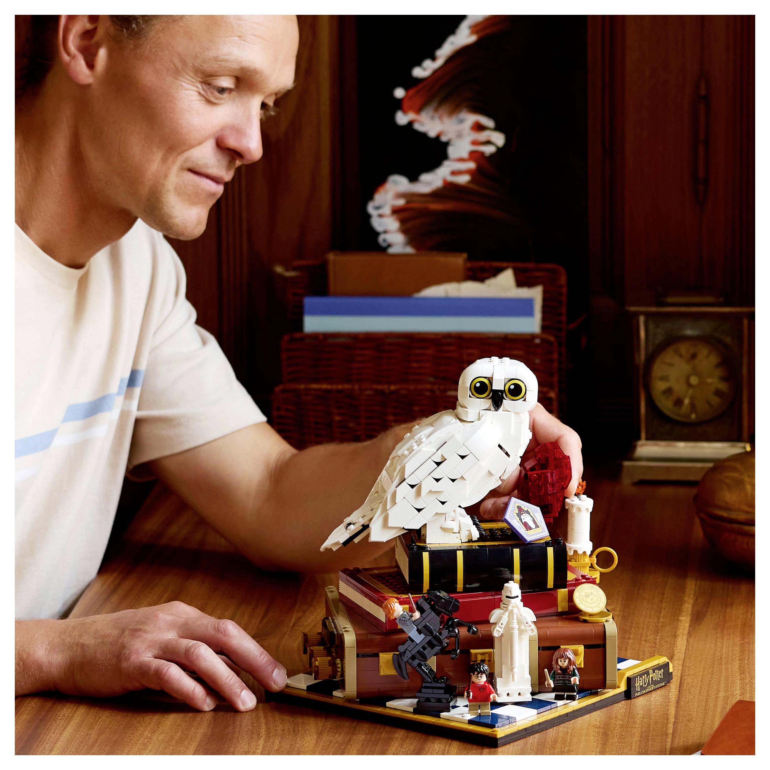 Une personne interagit avec un ensemble LEGO détaillé comprenant un hibou blanc, des livres empilés et diverses petites figurines sur une table en bois.