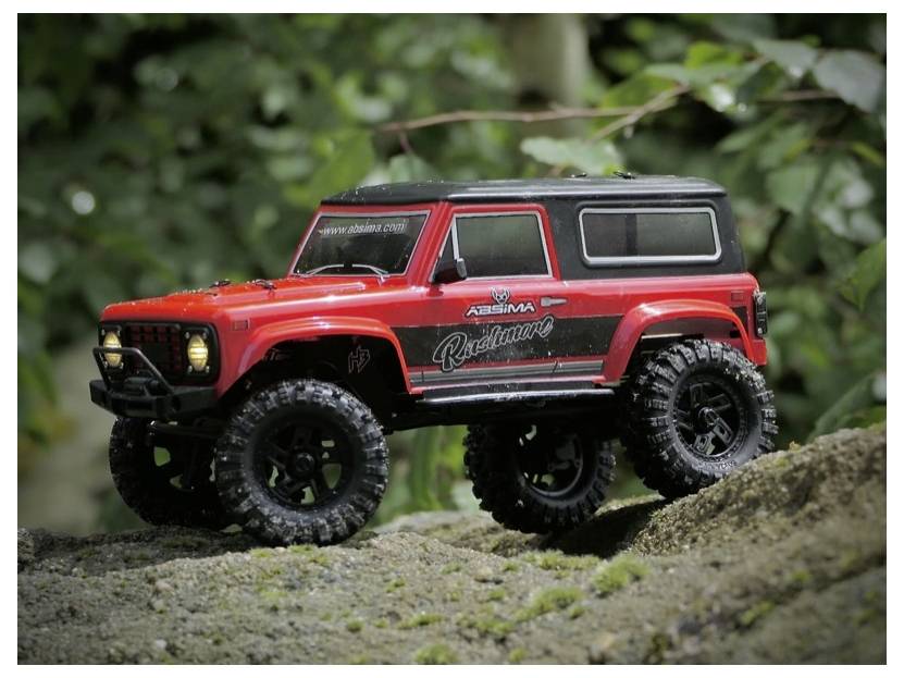 Un véhicule tout-terrain télécommandé rouge et noir sur un chemin de terre entouré de feuillage vert.